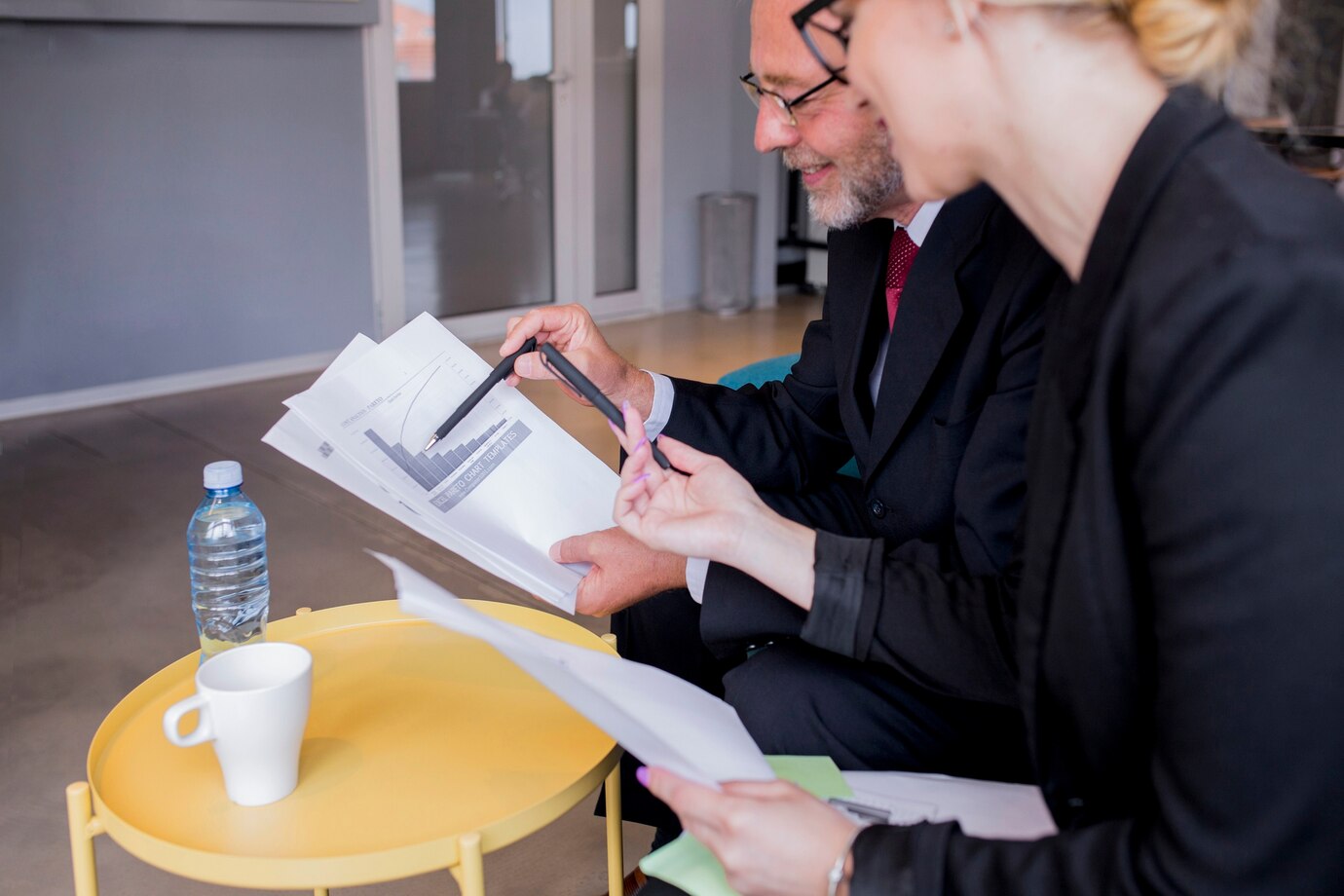 Business man and woman sitting at a desk, discussing financial reports and energy savings solutions.